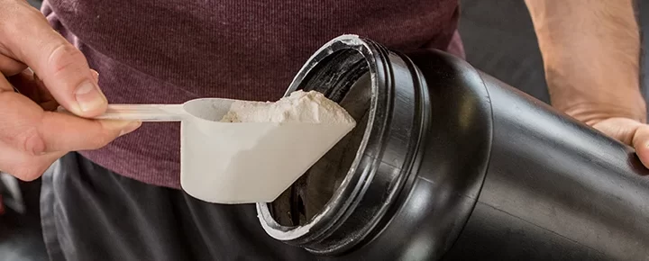 A person taking a scoop from a supplement container