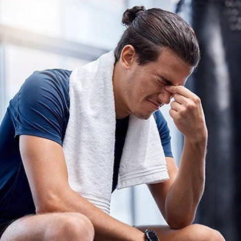 A man sitting in the gym experiencing headache as a side effect
