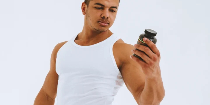 A bodybuilder holding a bottle of supplement