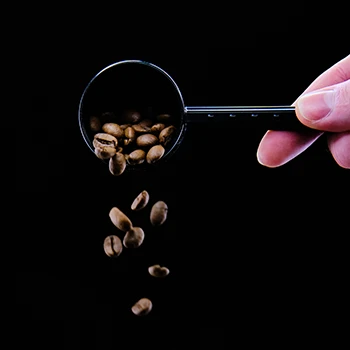 A hand pouring a scoop of coffee beans containing caffeine